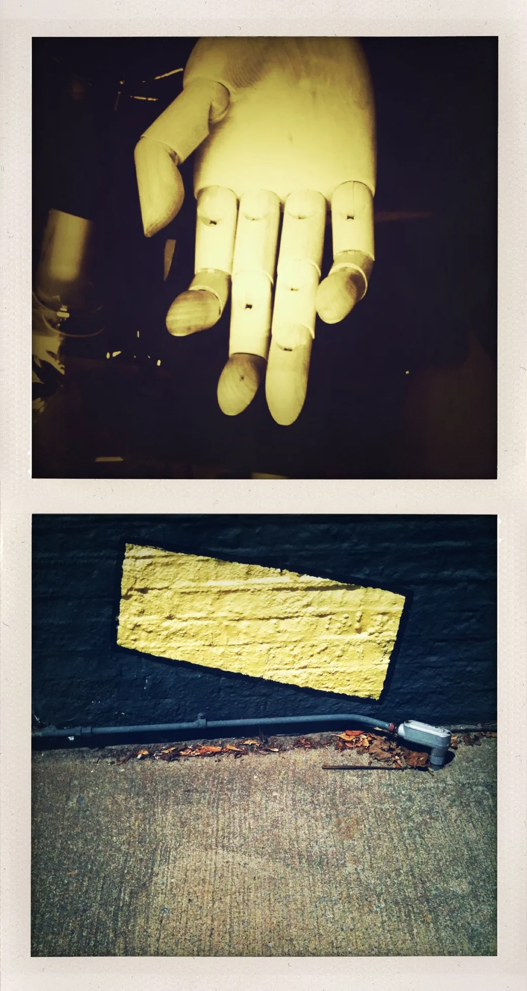 A wooden mannequin hand above a yellow painted rectangle on a brick wall, separated by a horizontal border.
