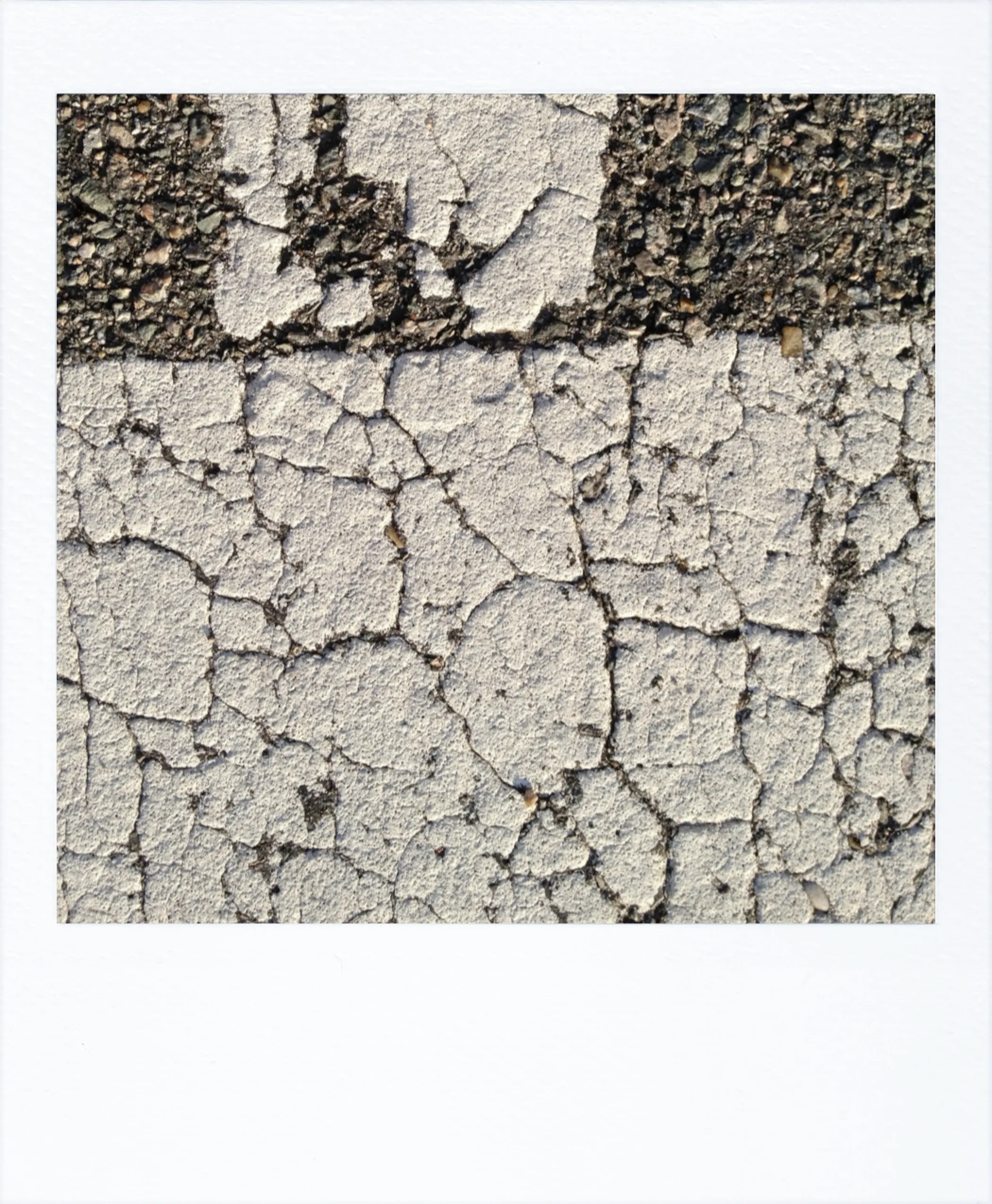 Close-up of cracked, weathered white paint on asphalt; broken lines resemble fragmented pavement or decaying signage.
