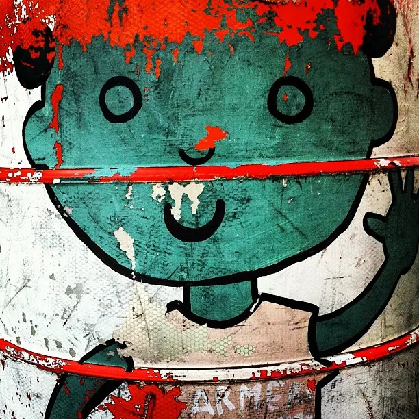 Close-up of a weathered and peeling illustration of a smiling child on a painted metal surface, partially obscured by red horizontal bars.