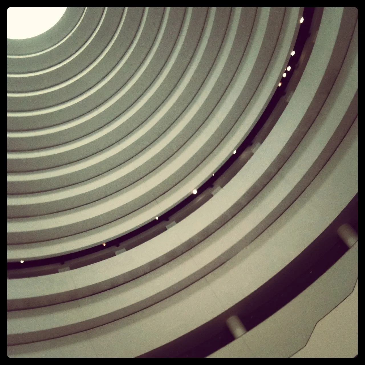Upward view of a modern building’s interior with concentric curved balconies forming a spiral pattern toward a circular skylight.