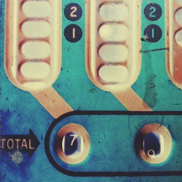 Close-up of a vintage blue and cream-colored mechanical counting device, showing labeled columns of white plastic buttons and a total display reading “70.”