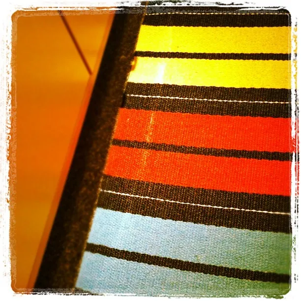 Close-up of a colorful woven fabric with horizontal stripes in yellow, red, blue, and black on a chair or bench.