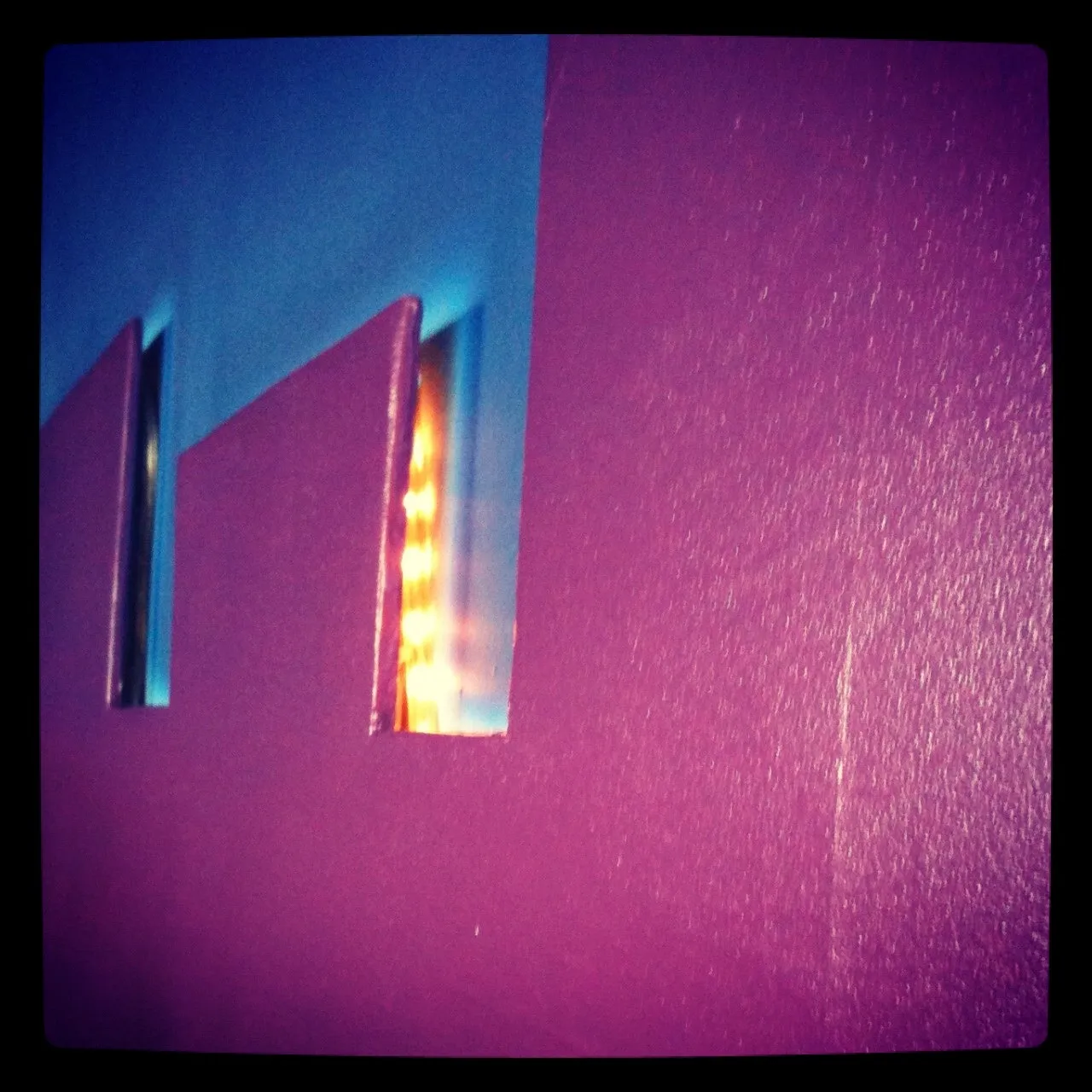 Close-up of a textured purple surface with rectangular cutouts revealing blue and orange light glowing through from behind.