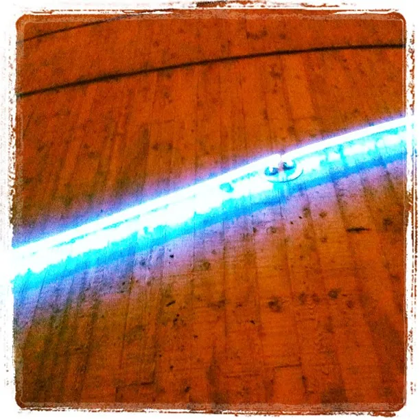 Bright blue neon light strip installed diagonally across a wooden floor, casting a vivid glow on the surrounding surface.