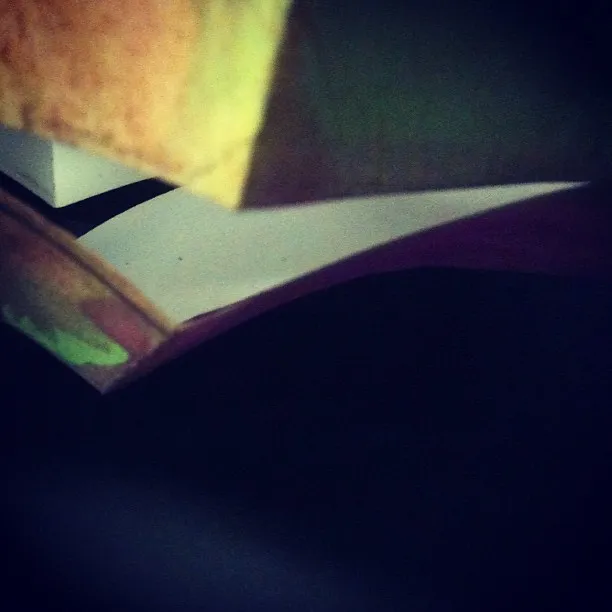 Close-up of folded and layered paper with painted edges in yellow and green tones, casting shadows on a dark background."