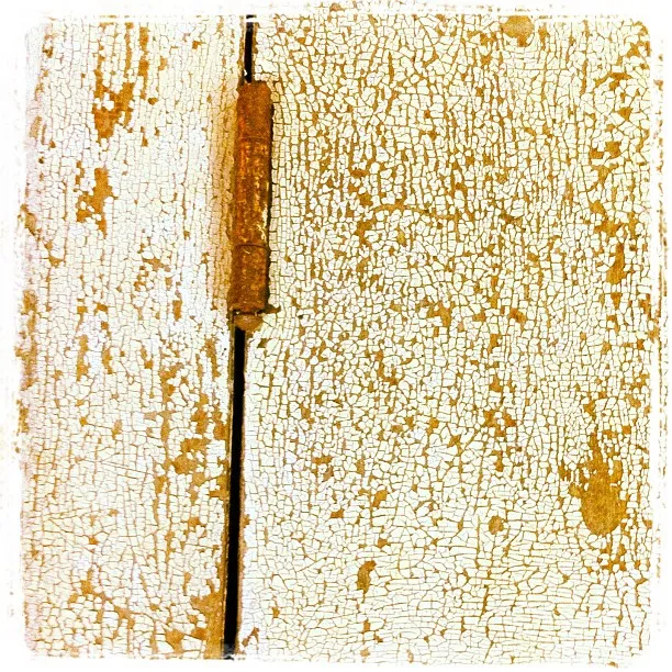 Close-up of a rusty hinge on a weathered wooden door with peeling and cracked white paint.