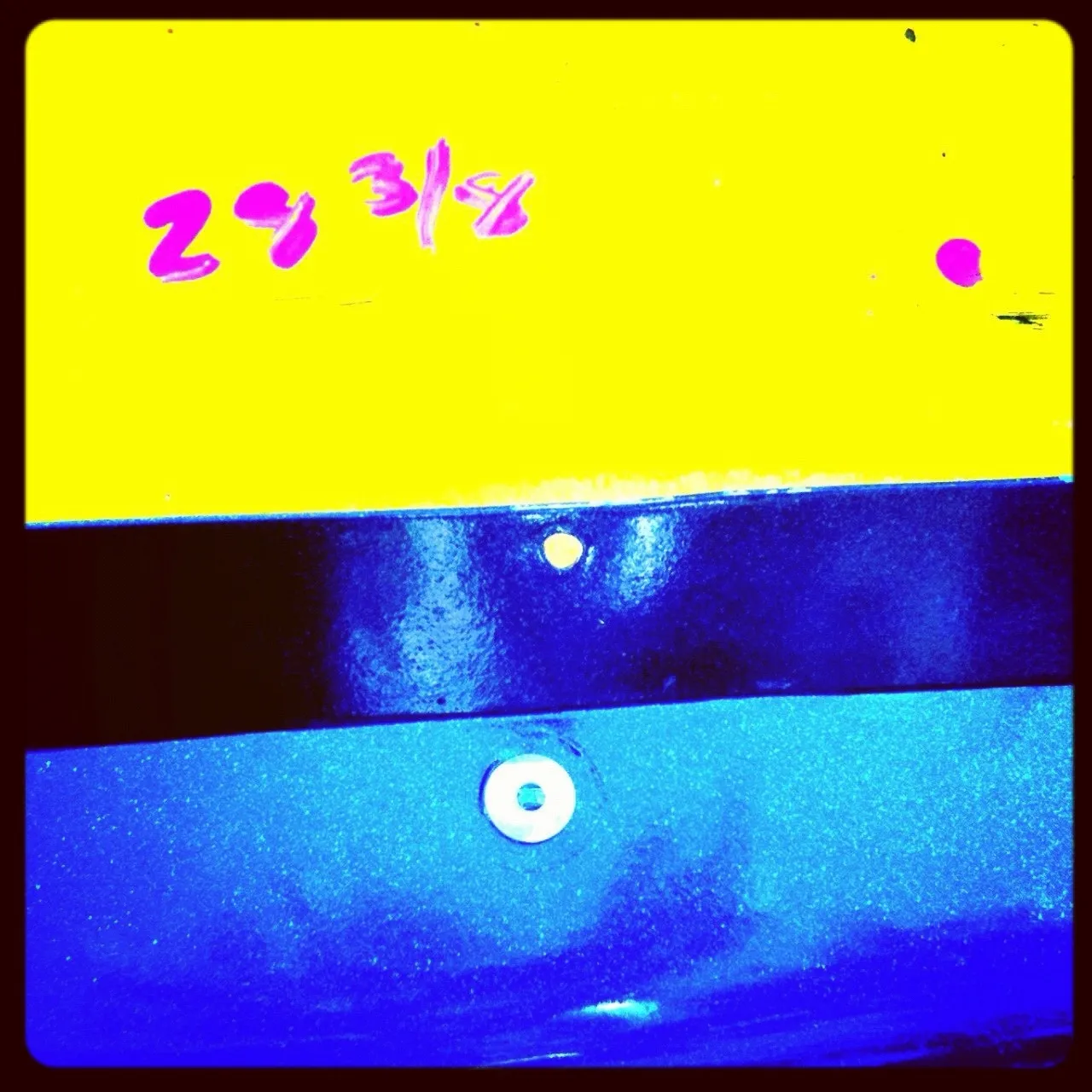 Close-up of a color-blocked metal surface with yellow, black, and blue sections, featuring handwritten red text “29 3/8” and visible screw heads.