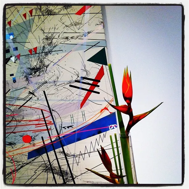 Colorful abstract artwork with geometric lines and shapes, alongside two tropical bird-of-paradise flowers in a clear vertical vase.