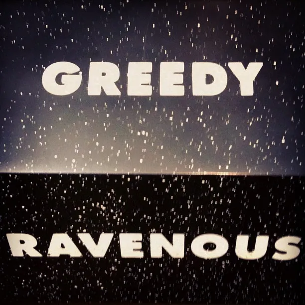 White block letters spelling “GREEDY” and “RAVENOUS” appear on a black and dark blue background, speckled with scattered white dots like stars.