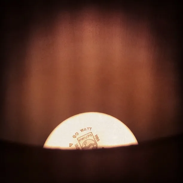 View from inside a lampshade looking down at the top of a glowing 60-watt light bulb with brand markings visible.
