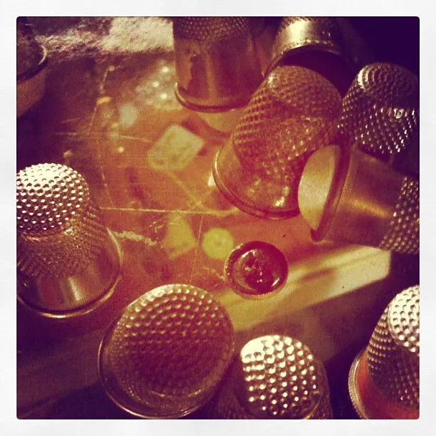Close-up of several metal thimbles arranged on a reflective surface, with warm lighting and visible dust or scratches.