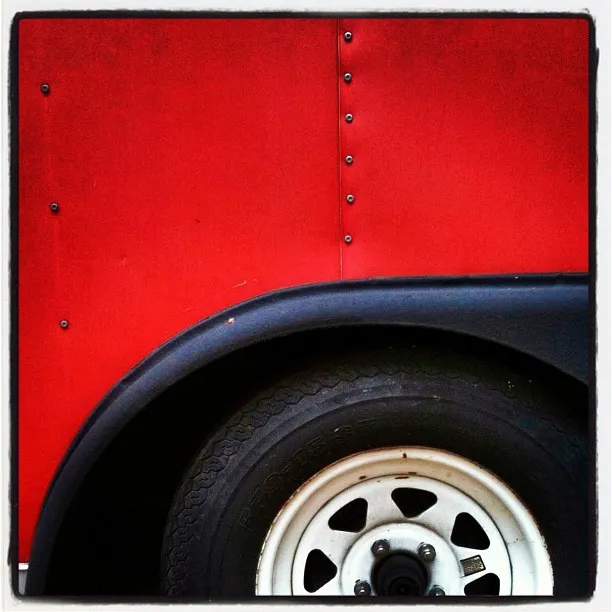 Close-up of a red trailer with black wheel well and white-rimmed tire, showing rivets and clean lines.