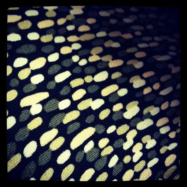 Close-up of textured fabric with a pattern of scattered beige, white, and olive dots on a dark background.