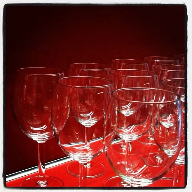 Clear wine glasses arranged in rows on a red shelf with reflections visible on the glass surfaces.