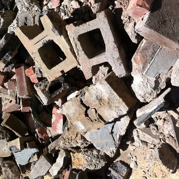 Pile of broken concrete blocks, bricks, and rubble in sunlight, showing varied textures and debris shapes.