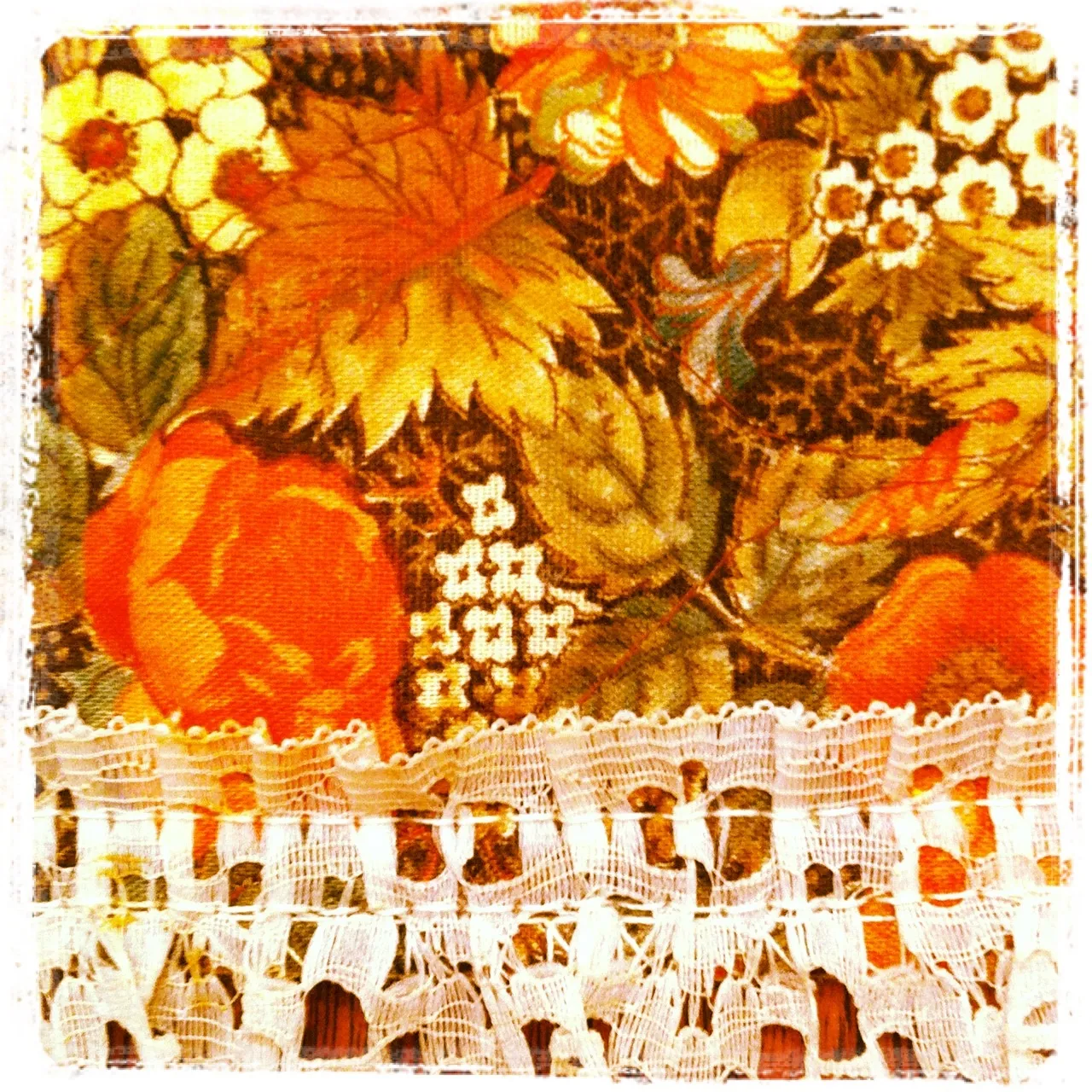 Close-up of vintage floral fabric in warm autumn tones with a horizontal band of white lace trim across the bottom.