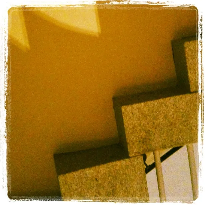 Close-up of a staircase with rectangular concrete steps against a yellow wall, creating geometric shadows and angular lines.