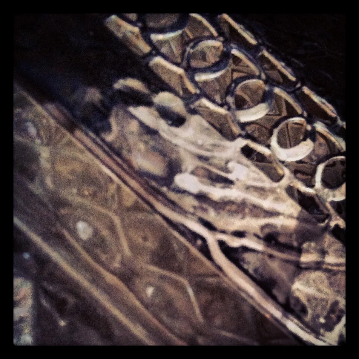 Close-up of overlapping patterned surfaces, including a textured mesh and hexagonal motifs, creating an abstract composition in muted tones.