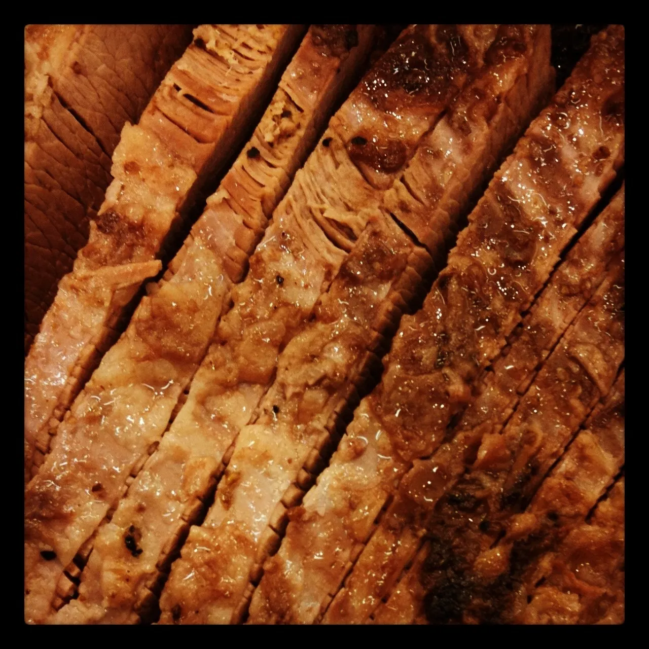Close-up of several slices of cooked, juicy brisket arranged in parallel, showcasing layers of meat, fat, and charred edges.
