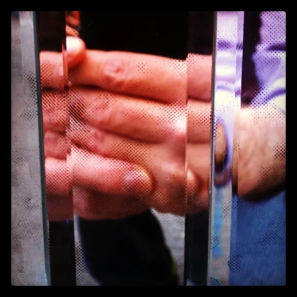 Close-up of hands clasped together behind a glass surface with vertical ridges and dotted textures, distorting the view.