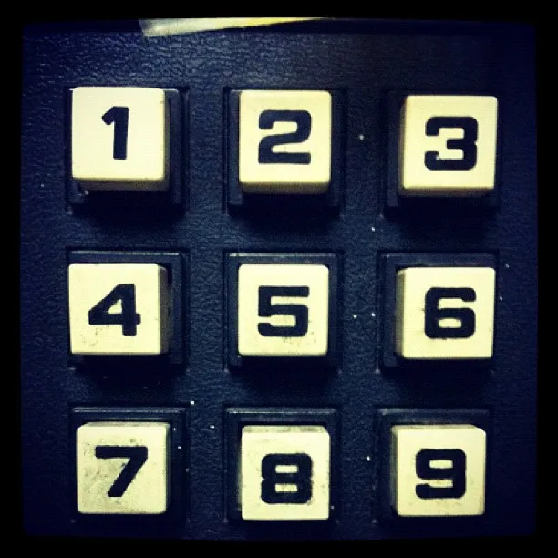 Close-up of a vintage numeric keypad with white keys labeled 1 through 9 on a dark background.