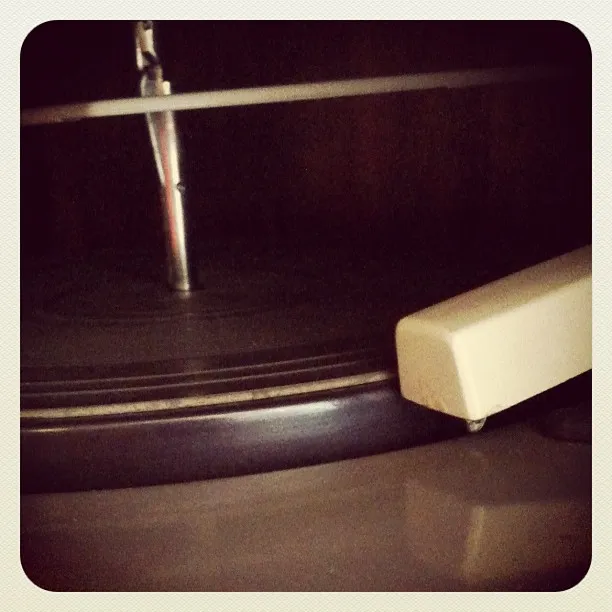 Close-up of a vintage record player turntable with part of the tonearm and platter visible in low lighting.