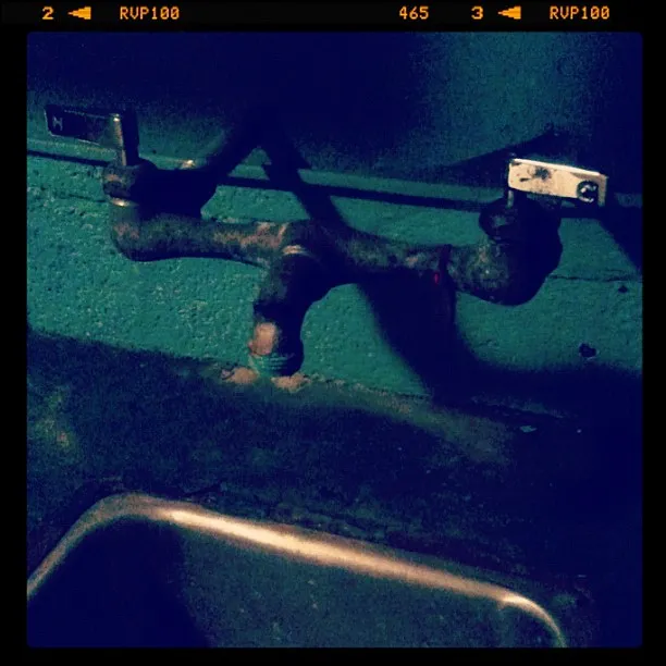 Rusted metal faucet with separate hot and cold handles mounted on a teal wall above a metal sink.