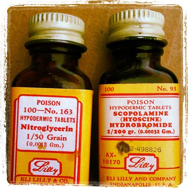 Close-up of two vintage amber glass medicine bottles labeled as poison, containing nitroglycerin and scopolamine tablets from Eli Lilly & Co.