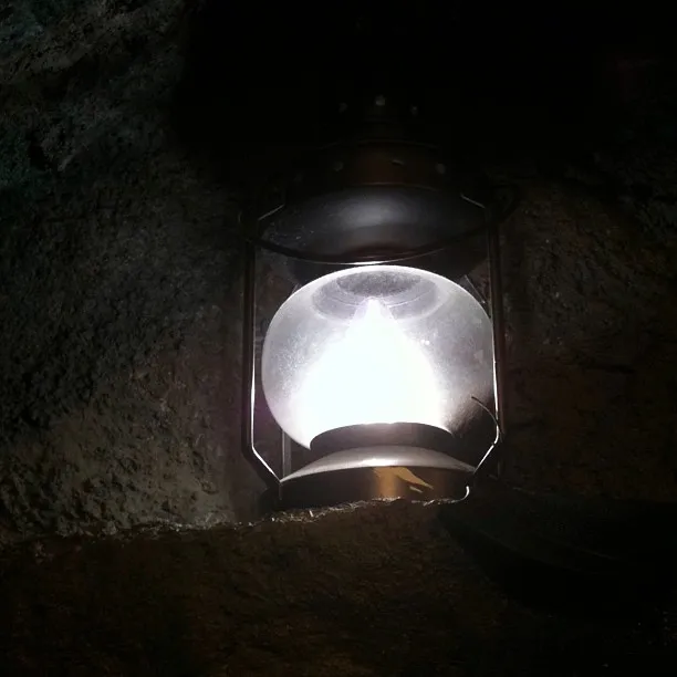 A wall-mounted metal lantern with a visible bulb glows brightly, casting light against a textured dark stone surface.
