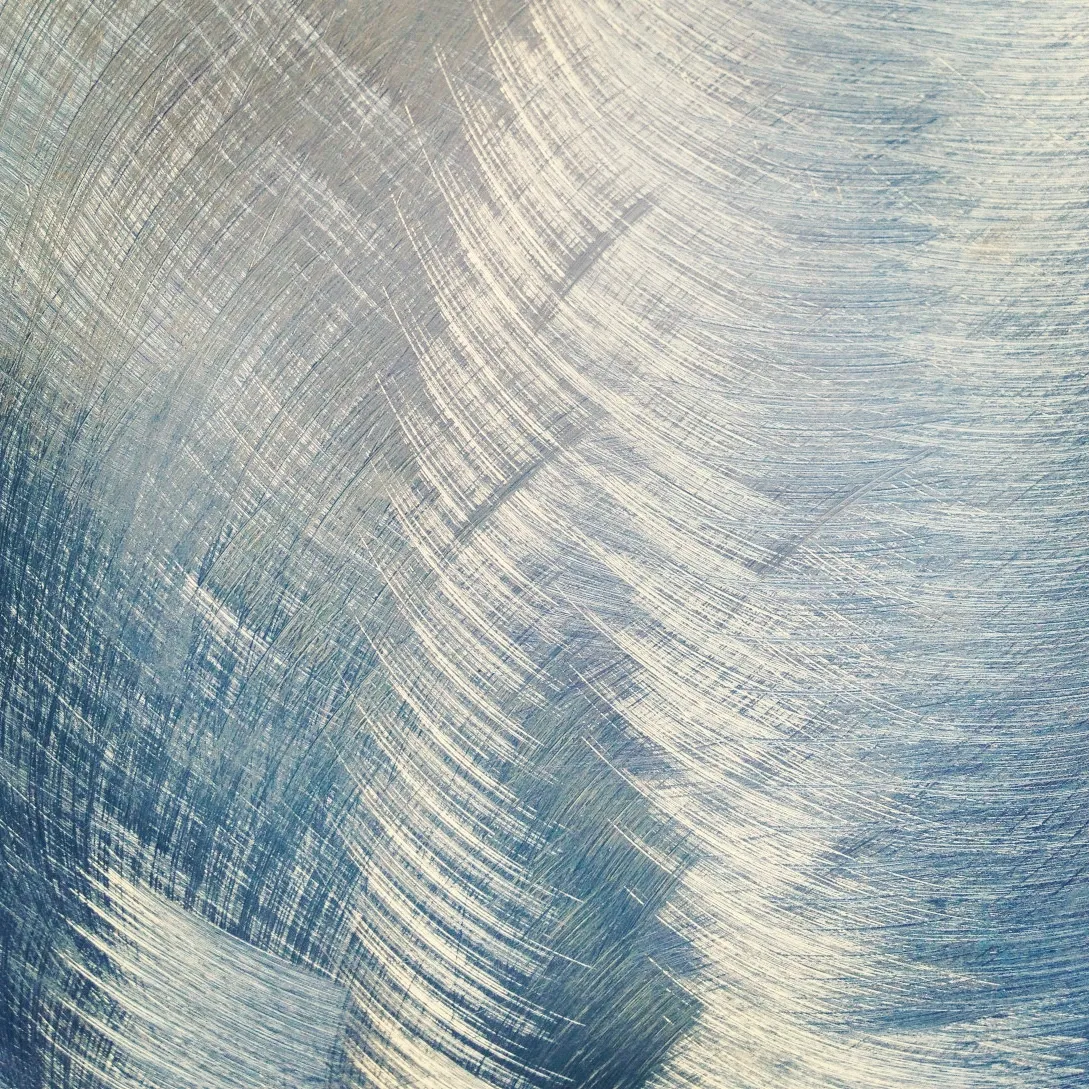 Close-up of brushed metal surface with overlapping curved strokes, creating a textured pattern in silver and blue tones.