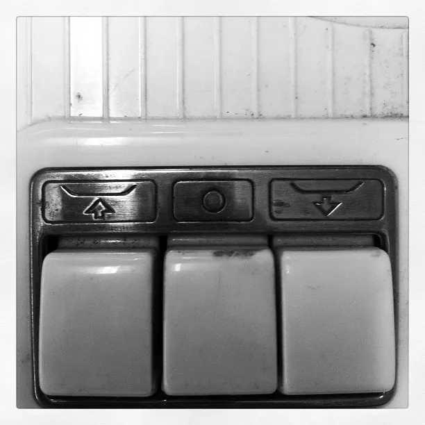 Close-up of three white plastic buttons on a wall switch panel, labeled with up, stop, and down arrow icons.