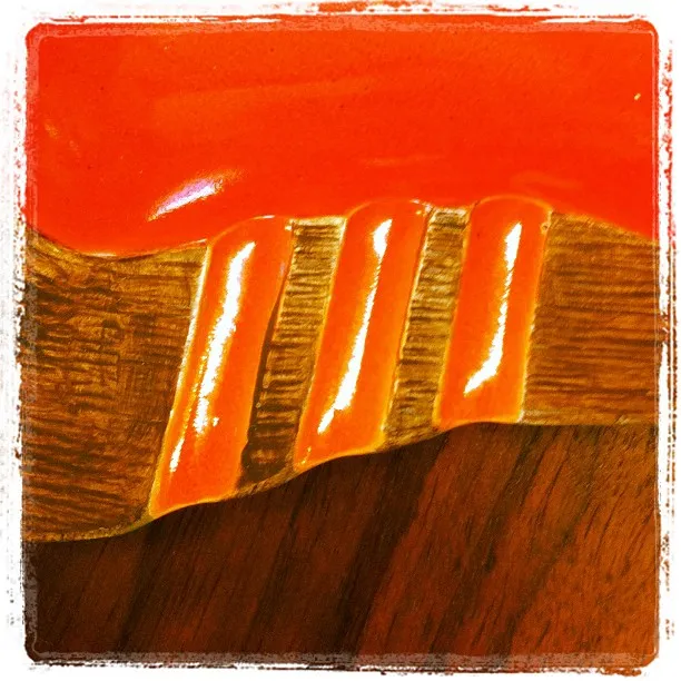 Close-up of a glossy, textured ceramic surface with red-orange glaze and raised ridges over a woodgrain-like base.