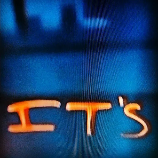 Close-up of a screen displaying the text “IT’S” in orange, with visible scan lines and a blue background suggesting a low-resolution video source.