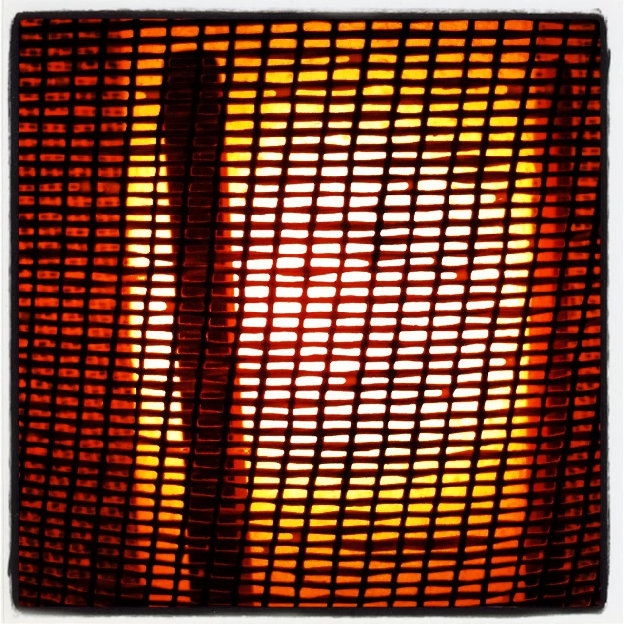 Close-up of a glowing light source behind a red-orange grid-like mesh, creating a warm, abstract geometric pattern.