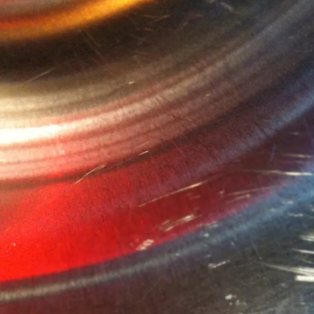 Close-up of a scratched metallic surface with circular patterns and reflections of red, yellow, and white light.