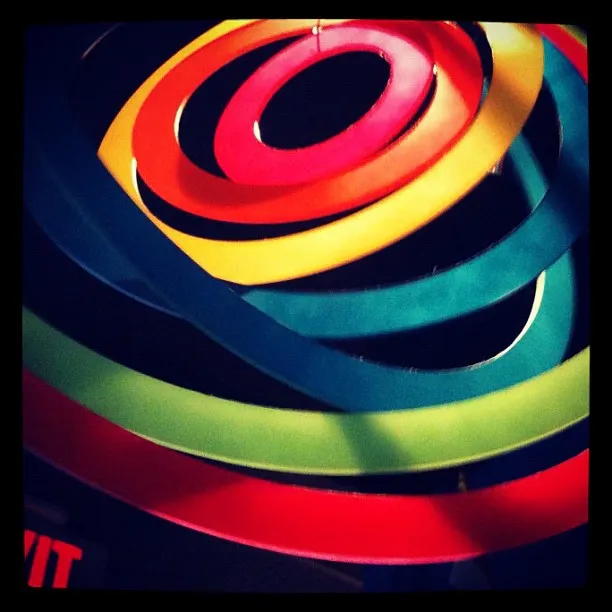 Overhead view of a hanging spiral sculpture made of colorful concentric rings in red, orange, yellow, green, and blue.