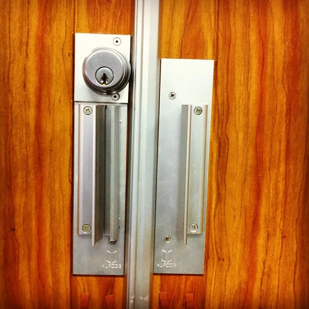 A close-up of a metal door lock and handle set mounted on a wood-paneled door with brushed aluminum components.