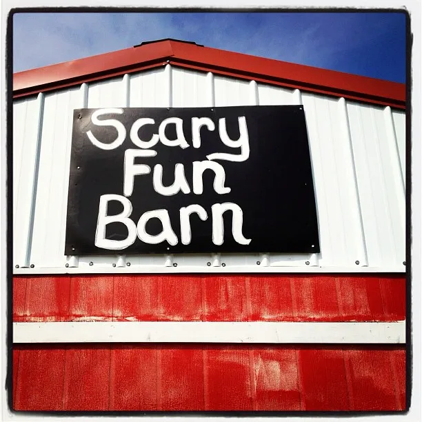 Red and white barn with a hand-painted black sign that reads “Scary Fun Barn” in white letters.
