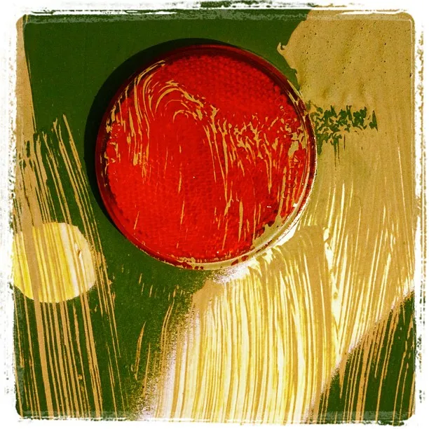 Close-up of a red circular reflector on a green painted surface with smudged yellow and white streaks across it.