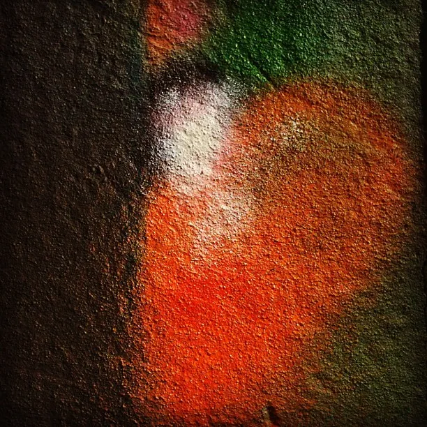 Close-up of a textured wall with spray-painted abstract shapes in red, orange, green, white, and black tones.