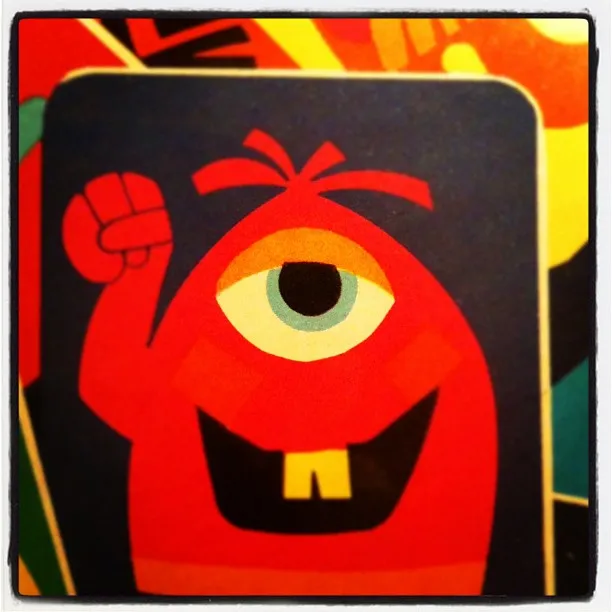 Illustration of a red, one-eyed cartoon monster with a raised fist, a single tooth, and a cheerful expression on a card.