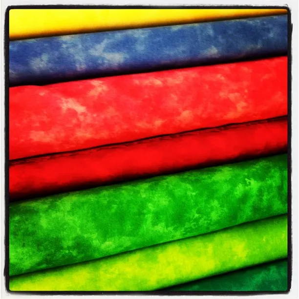 Stack of brightly colored marbled fabrics in yellow, blue, red, and green tones, arranged in horizontal layers.