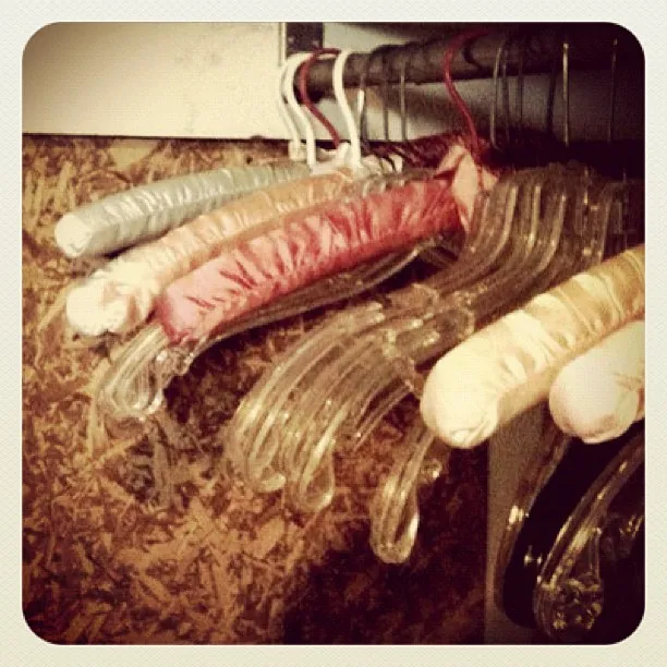 Close-up of a row of padded satin and clear plastic clothes hangers hanging on a metal rod against a textured wooden wall.