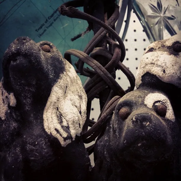 A close-up of weathered dog-shaped sculptures with peeling paint, surrounded by twisted metal wires and a perforated white background.