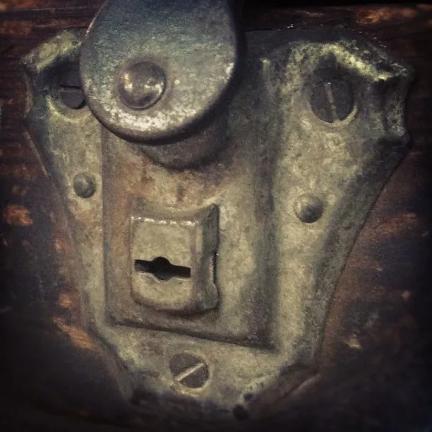 Close-up of an old, weathered metal lock plate with a keyhole, mounted on a wooden surface.