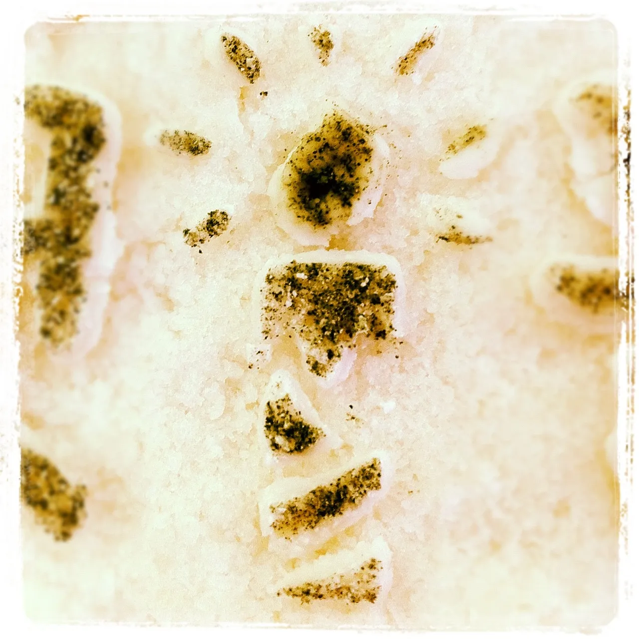 Close-up of white granular surface, possibly salt, with shapes resembling a sun and abstract symbols outlined in black pepper.