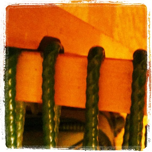 Close-up of green plastic-coated cords looped over the edge of a wooden surface, with warm lighting and a slightly grainy texture.