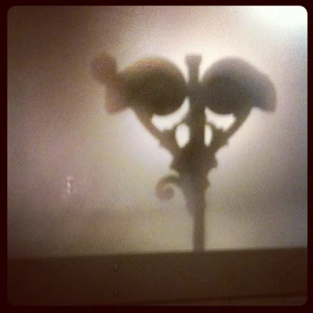 Silhouetted streetlamp with ornate design barely visible through a foggy or frosted window, creating a moody effect.