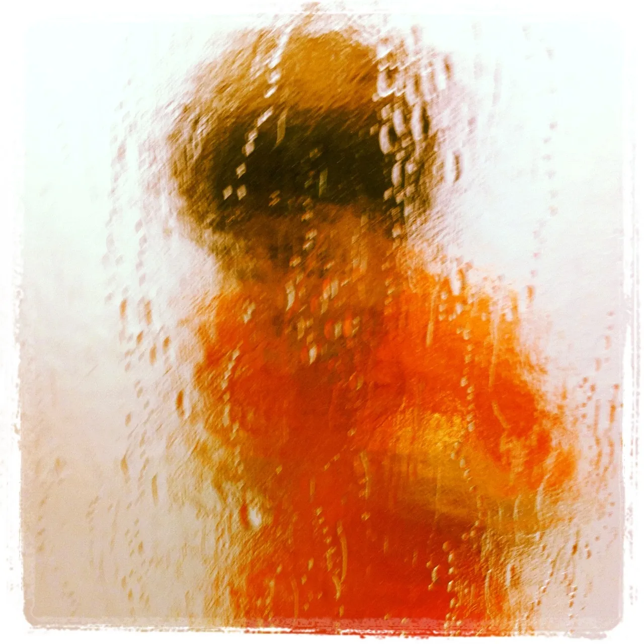 Blurry silhouette of a person in an orange garment seen through a textured, condensation-covered glass surface.
