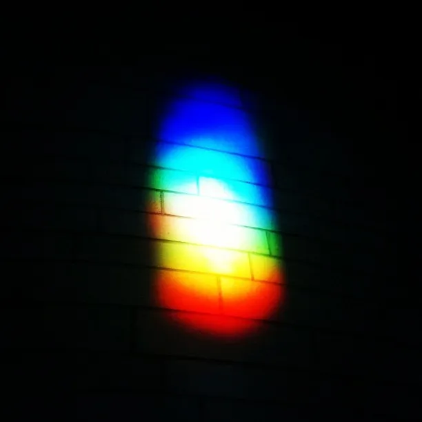 A vertical rainbow-colored light projection on a tiled wall in a dark setting.